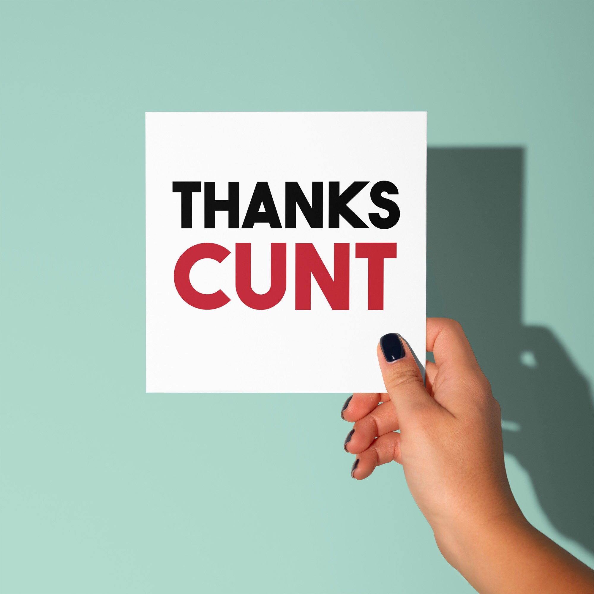 Hand holding a card with 'THANKS CUNT' text against a light green background